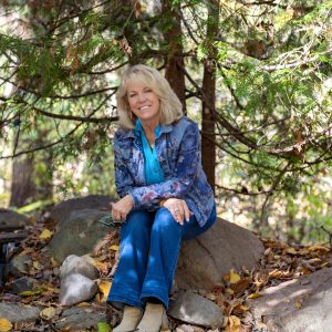 Jennifer Mercier sitting on a boulder in the woods.